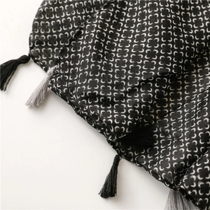 Detail of black geometric scarf featuring white crescent patterns and elegant grey tassels