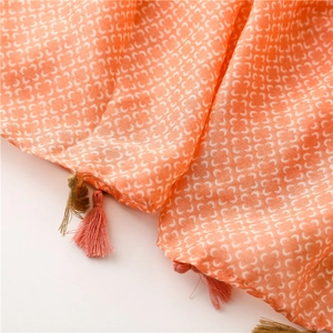 Macro detail of peach scarf showing white clover patterns and delicate two-tone tassels