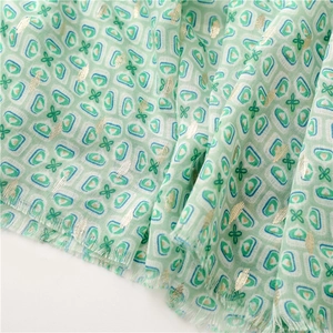 Close-up of light green geometric scarf with gold foil dots and fringe edges