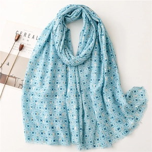 Close-up of light blue cotton-linen scarf with geometric gold patterns and fringe edges