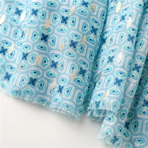 Macro view of light blue cotton-linen scarf featuring floral print and gold foil stripes