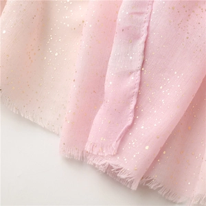 Macro detail of pink lightweight fabric with gold foil polka dots and raw fringe edge
