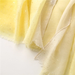 Close-up of light yellow gradient scarf with gold glitter texture and frayed edges