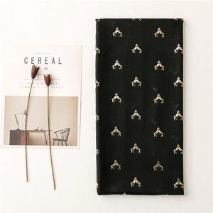 Detail of black cotton scarf featuring golden reindeer antler patterns on white background