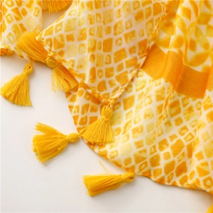Detail of yellow geometric kaleidoscope scarf with decorative tassel fringe on white background