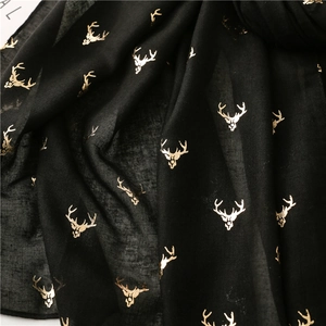 Detailed view of black scarf featuring gold reindeer head patterns and rolled edges