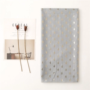 Detail of light gray scarf featuring golden rhombus patterns and soft textile texture