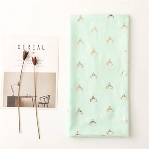 Detail of mint green scarf with golden reindeer prints next to a lifestyle magazine