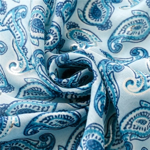 Macro detail of light blue paisley fabric with silver metallic threads and soft folds