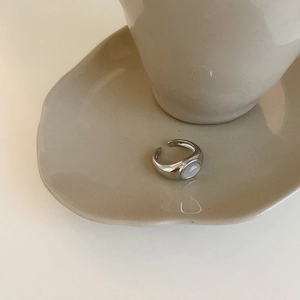 Detailed view of silver adjustable ring with white oval cat eye stone on ceramic dish