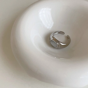 Detail view of a silver open ring with white oval opal inlay on a white circular stand