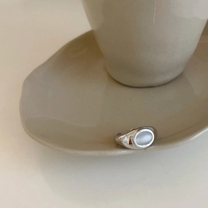 Detail of silver cat-eye stone ring placed on minimalist ceramic tea set for an elegant look