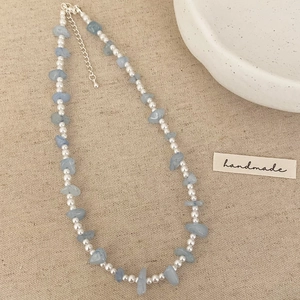 Détail d'un collier artisanal avec petites perles blanches et pierres bleues claires