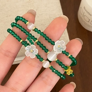Détail du bracelet multicouche en cristal vert avec fleurs blanches et nœud doré