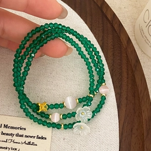 Détail du bracelet multicouche en perles vertes avec papillon doré et fleurs
