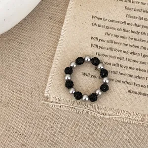 Détail de bague perlée avec perles argentées et noires sur fond en lin texturé vintage