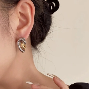 Gros plan de boucles d'oreilles créoles bicolores entrelacées portées par un mannequin