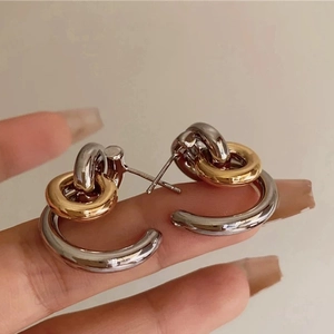 Détail des boucles d'oreilles créoles bicolores entrelacées au design géométrique poli