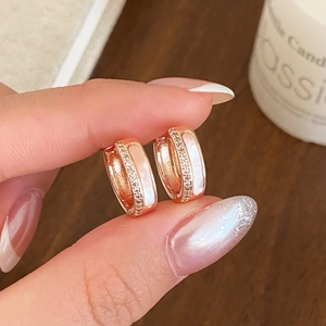 Gros plan de boucles d'oreilles créoles dorées à l'or rose avec zircon et nacre
