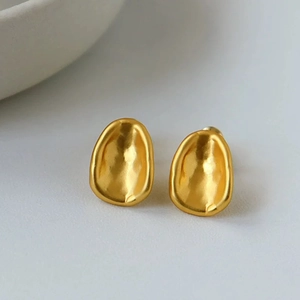 Detailed view of matte gold oval stud earrings with organic hammered metal texture