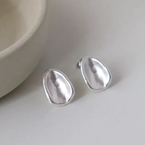 Macro detail of organic irregular oval silver stud earrings with a matte brushed finish