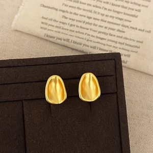 Detail of matte gold concave oval stud earrings on vintage fabric background