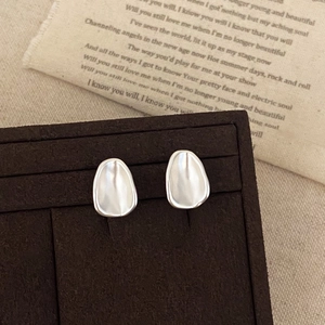 Detailed view of irregular organic oval stud earrings in matte silver finish on fabric