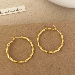 Elegant gold twisted hoop earrings with textured matte finish on craft paper background