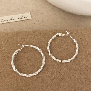 Elegant twisted silver hoops with frosted texture on handmade craft display board