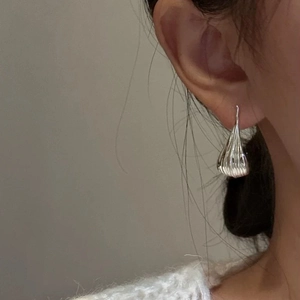 Minimalist silver teardrop earrings with textured vertical pleats on a female model