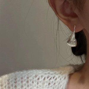 Close-up of teardrop-shaped silver metal earrings with textured vertical grooves on ear