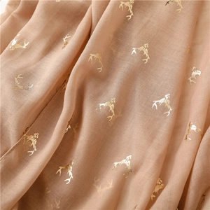 Close-up of lightweight beige scarf featuring elegant gold foil reindeer prints