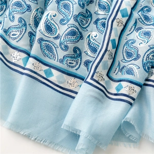 Detail of light blue paisley scarf featuring silver foil accents and delicate fringe edges
