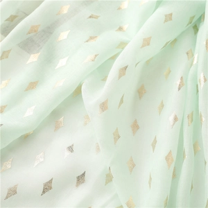 Close-up of mint green scarf fabric with gold foil diamond patterns and texture