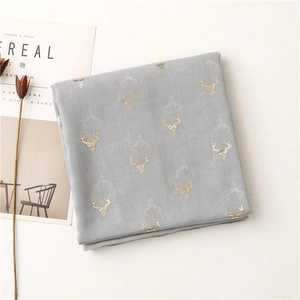 Detail of grey lightweight scarf with gold foil deer pattern next to lifestyle props