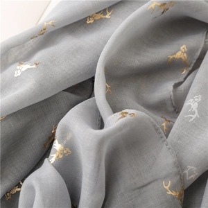 Detail of light gray cotton scarf with gold reindeer print and sheer woven texture