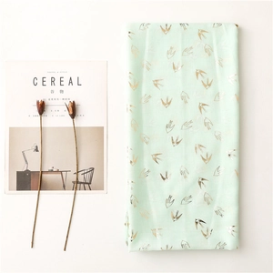 Close-up of mint green scarf with elegant gold foil swallow pattern on linen-feel fabric