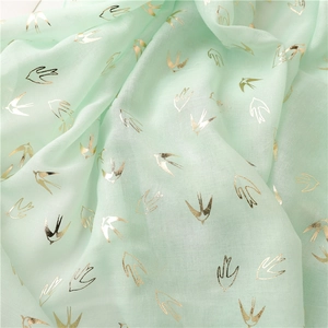 Macro shot of light green fabric with delicate gold swallow prints and soft texture