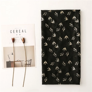 Detail of black cotton scarf with gold swallow print next to minimalist magazine and flowers