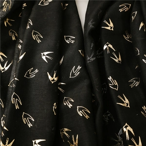 Detailed macro view of black cotton-blend scarf featuring metallic gold swallow prints