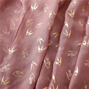 Detail of light pink linen-feel scarf featuring metallic gold swallow bird foil print