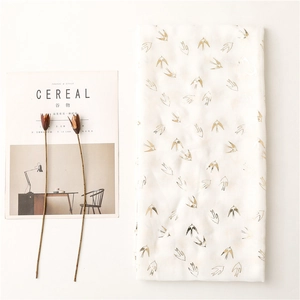 Detail of white scarf with gold swallow prints and soft texture on a minimal background