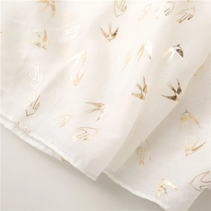 Close-up of lightweight white scarf featuring elegant gold foil swallow bird patterns