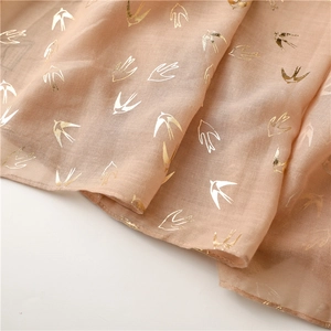 Macro detail of soft champagne scarf featuring elegant gold foil swallow bird prints