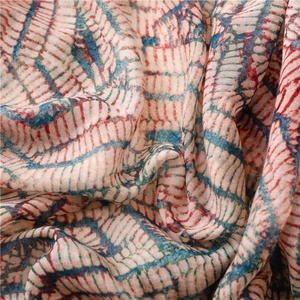 Détail d'écharpe ethnique montrant un motif géométrique rouge et bleu sur tissu beige