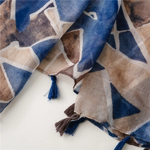 Detail of geometric watercolor print scarf with blue and brown tassels on light fabric