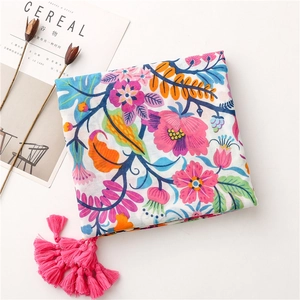 Close-up of floral cotton linen scarf with pink tassels and a decorative magazine background