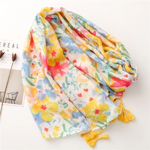 Beige cotton-feel scarf with tropical floral print and yellow tassels laid on flat background