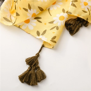 Detail of yellow daisy floral shawl featuring green woven tassels and cotton texture