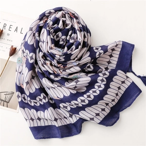 Detailed view of navy blue scarf with white geometric petals and tassel edges on white surface